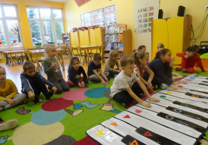 Dzieci grają na instrumencie kolor piano. Wokół nich siedzą dzieci przyglądające się z zainteresowaniem.